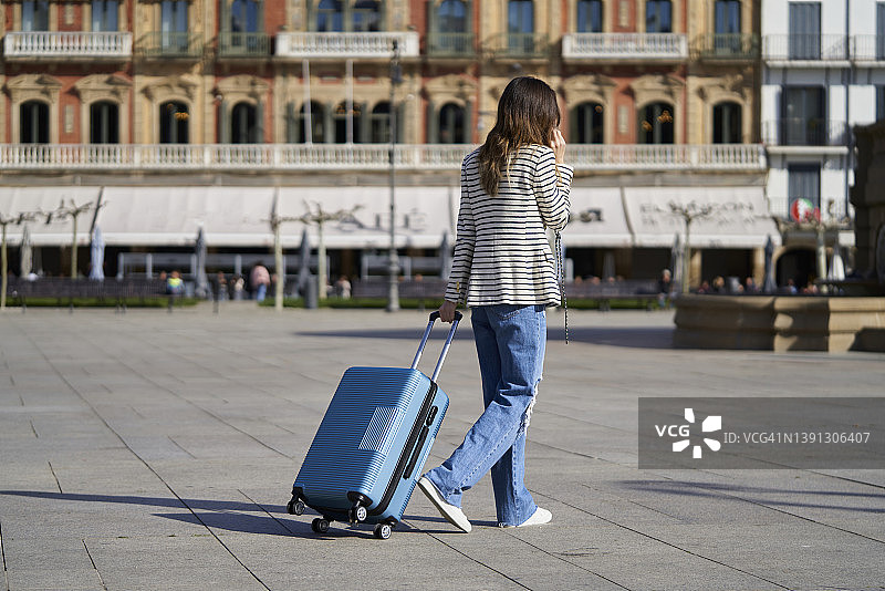 在一个广场上手提着手提箱，在阳光明媚的早晨前往欧洲度假酒店的年轻女子图片素材