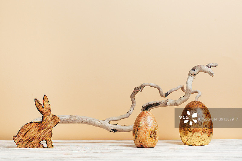 米色背景下的木制兔子和金色图案的木制彩蛋，生态复活节庆祝和春天的到来概念图片素材