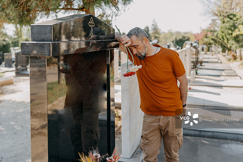 悲伤的中年男人在墓地墓碑旁悼念逝者图片素材