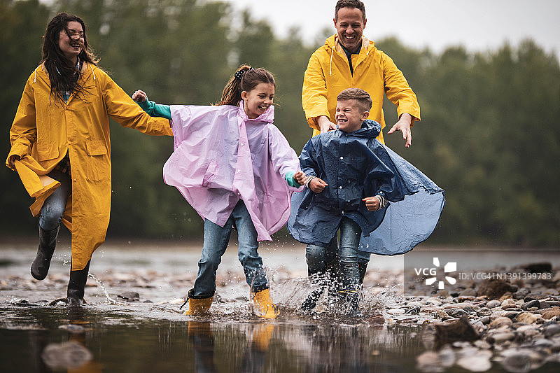 快乐的家庭穿着雨衣在雨中湖边嬉戏图片素材