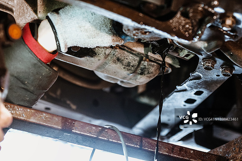 开放式机油滤清器的仰视角度。汽车修理工在车库更换机油图片素材