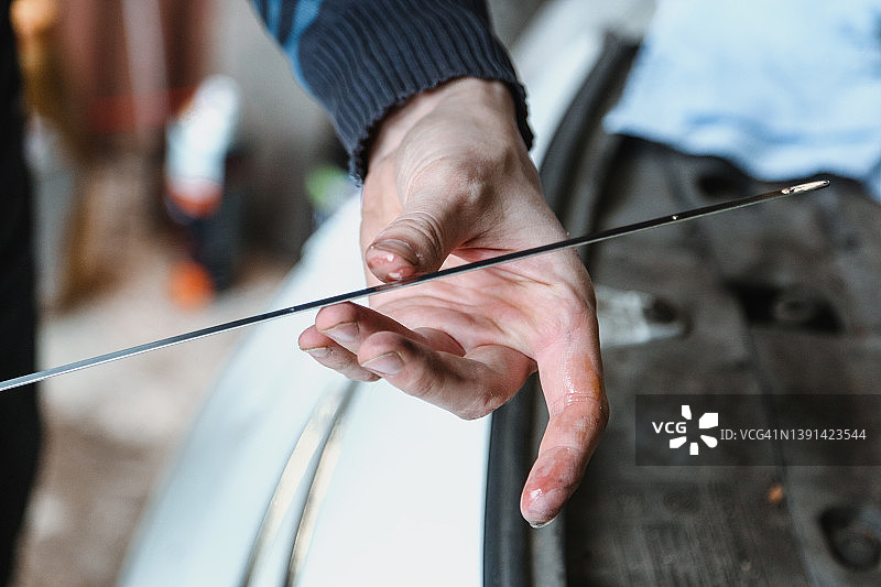 汽车修理工在车库修理汽车，使用油尺检查发动机油图片素材