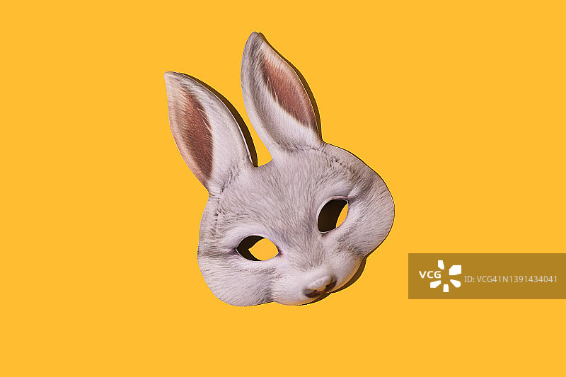 黄色背景上带有阴影的野兔面具：伪装、化装舞会、狂欢节、复活节和乐趣概念图片素材