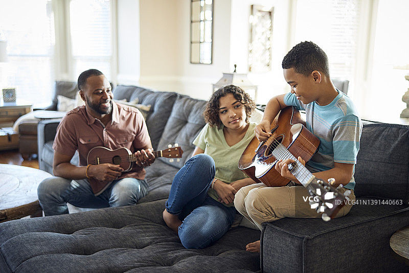 父亲、女儿和儿子在沙发上玩音乐。图片素材