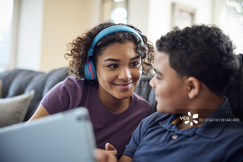 姐弟在客厅沙发上一起看平板电脑。图片素材