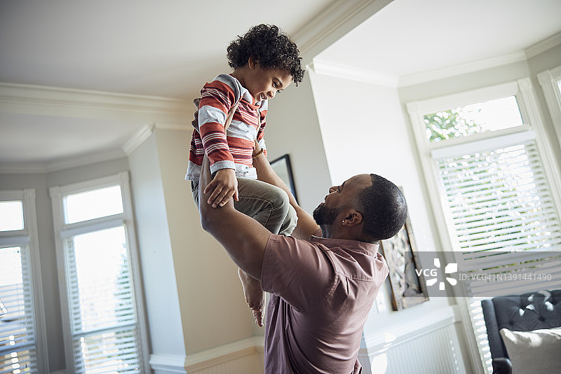 白天，非洲裔父亲在客厅里把儿子抱起来图片素材