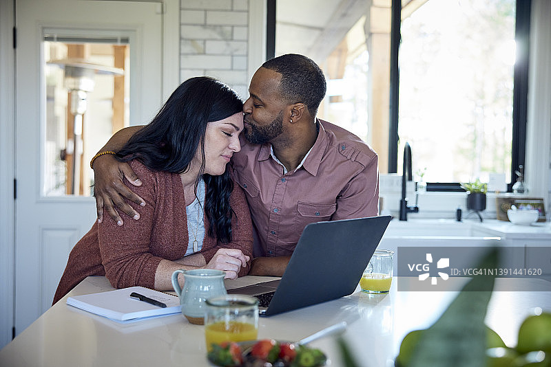 白人女子和非裔男子在厨房的柜台边一边吃早餐一边用笔、纸和笔记本电脑工作图片素材