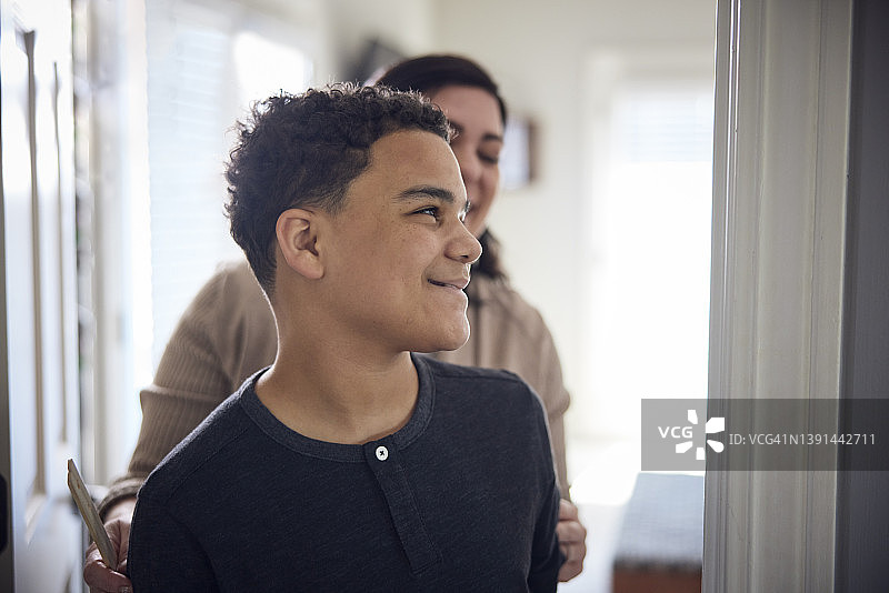 白人母亲在墙上量混血儿子的身高图片素材