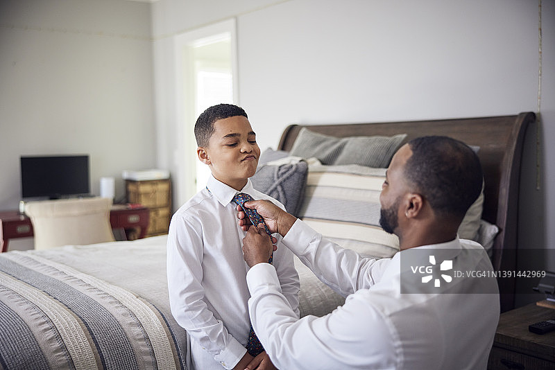 非裔美国父亲帮助混血儿子在卧室里穿衬衫和领带图片素材