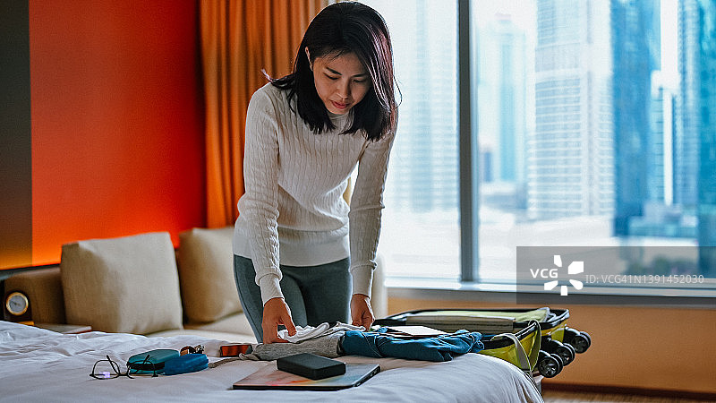 一位亚洲女性收拾行李箱准备离开公寓——独自旅行图片素材