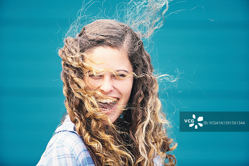 风中的秀发：一位美丽的卷发年轻女人在欢笑，风将她的长发缠绕在脸上图片素材