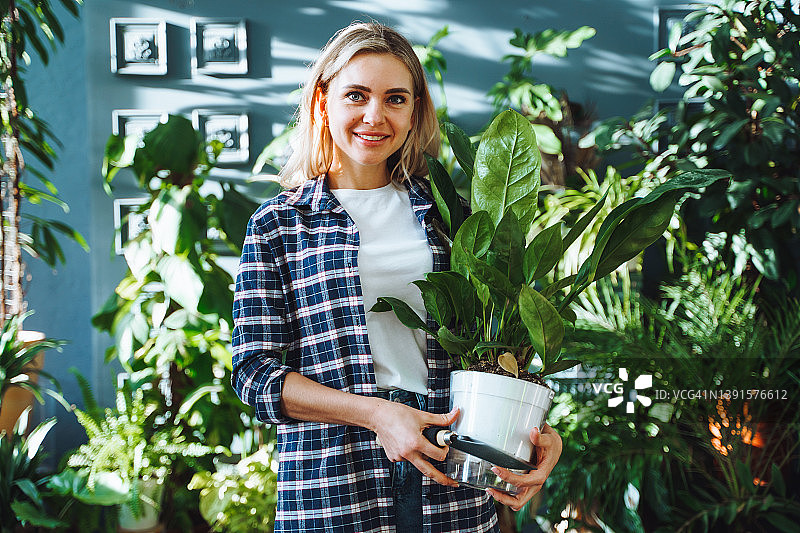 在花卉商店里拿着香草盆栽的年轻微笑金发女商人图片素材