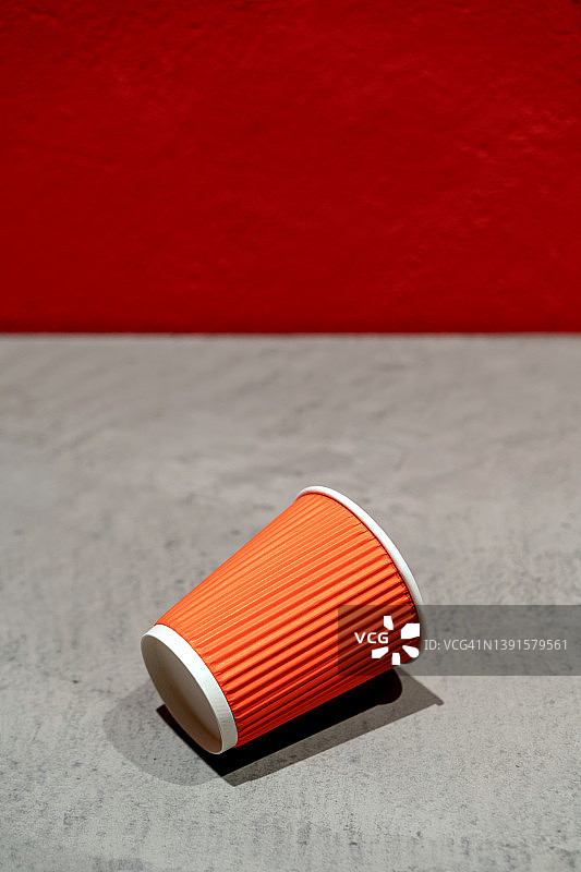 一次性红色瓦楞纸咖啡杯放在灰色水泥桌上，背景是彩绘墙。外卖咖啡，环境保护、回收利用概念。图片素材