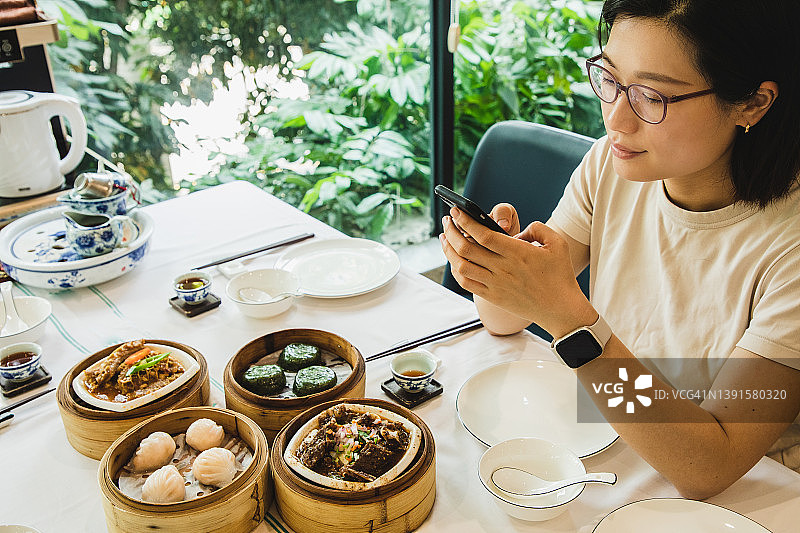 享用点心同时使用手机的亚洲女人图片素材