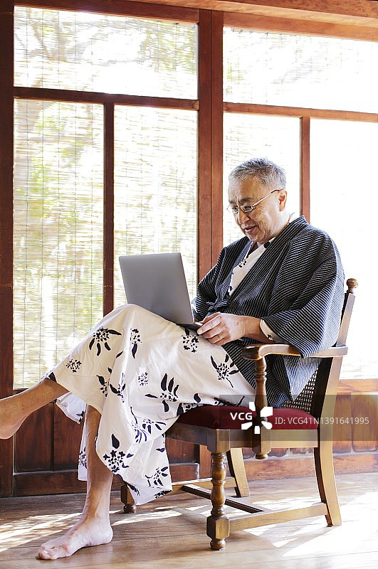 年老男性穿着日本浴衣“日本温泉袍”使用笔记本电脑图片素材