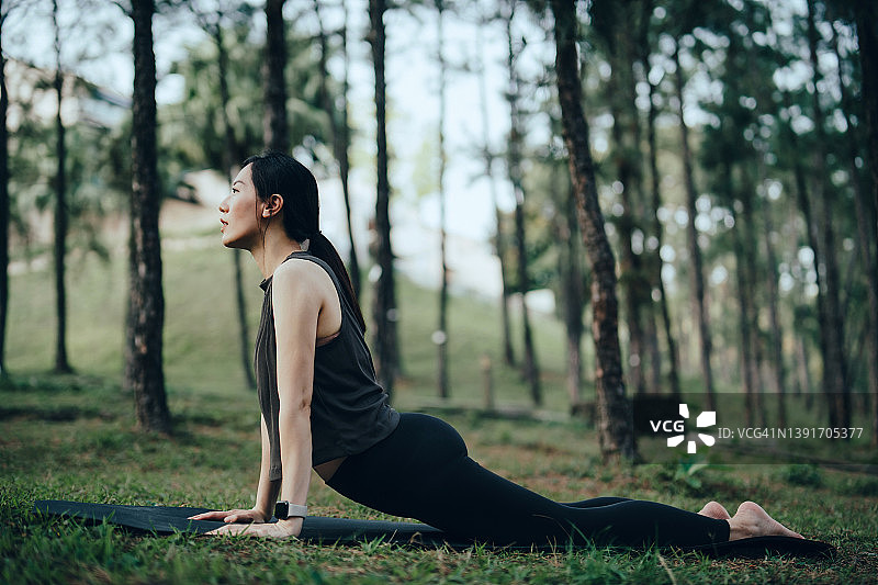 年轻亚洲女性在公园户外运动垫上练习瑜伽，做向上犬式。健身和健康的生活方式图片素材