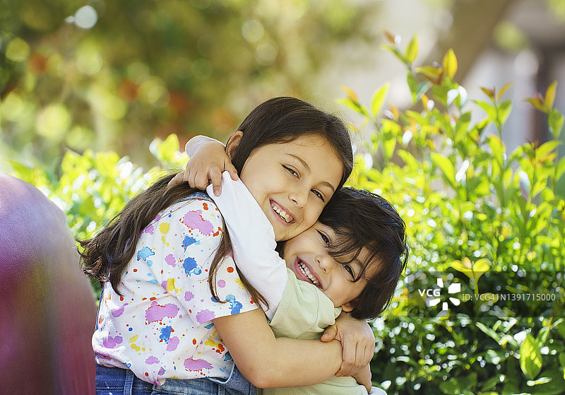 九岁姐姐在色彩缤纷的花园背景中拥抱她的弟弟图片素材