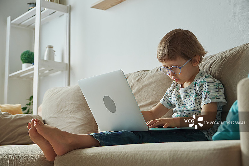 孩子在家用笔记本电脑在沙发上学习，远程教育图片素材