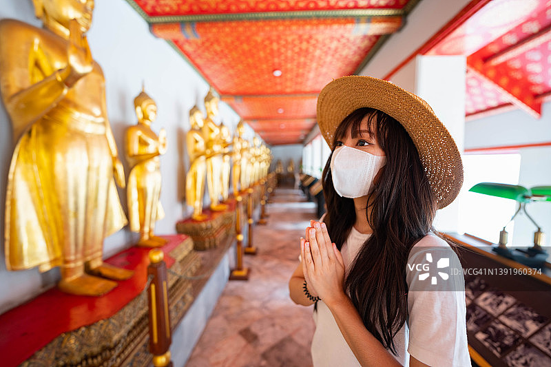 在泰国曼谷卧佛寺雕像前双手合十祈祷的快乐年轻亚洲女游客图片素材