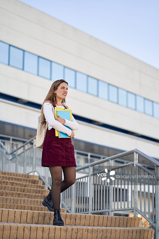 微笑的女人与文件夹和抄本在大学大楼的楼梯上图片素材