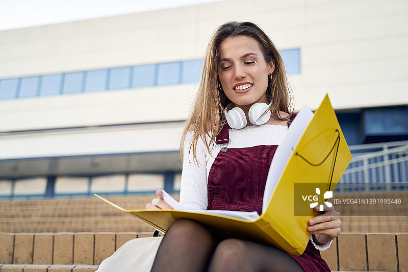 戴着无线耳机，在楼梯上阅读文件的女学生图片素材