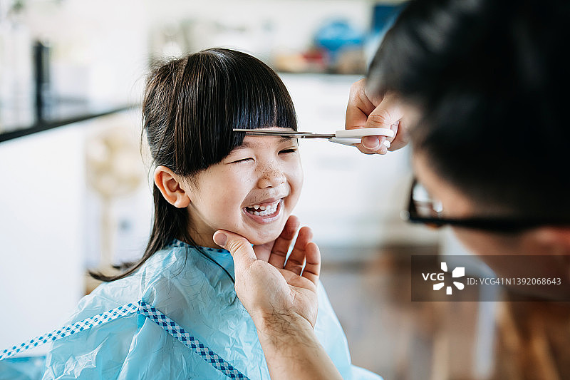 年轻的亚洲父亲在家为女儿理发，父女俩愉快地聊天图片素材