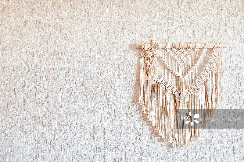 手工编织墙饰，木棍悬挂于白墙，棉线编织，女性爱好，环保现代针织内饰，留白图片素材