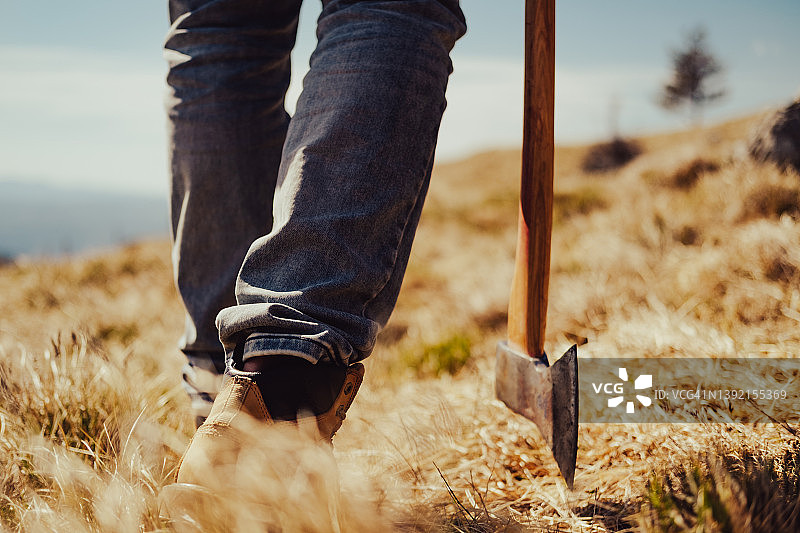 干燥草地上的脚部特写，男子独自站在山丘上，手持斧头图片素材