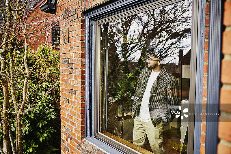 男子透过家里的窗户向外看的中景图片素材