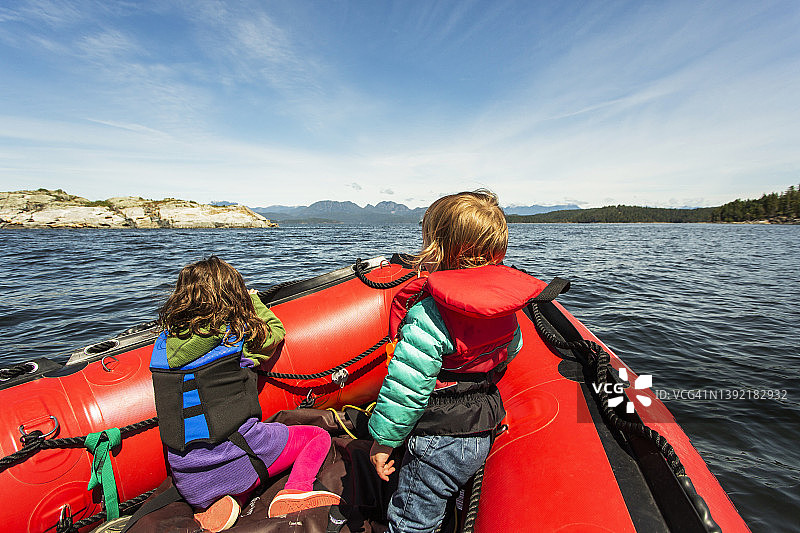 两个年轻的孩子坐在橡皮筏的船头看着岩石岛图片素材