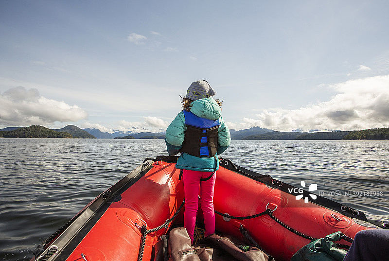 年轻女孩站在大海湾的橡皮艇船头图片素材