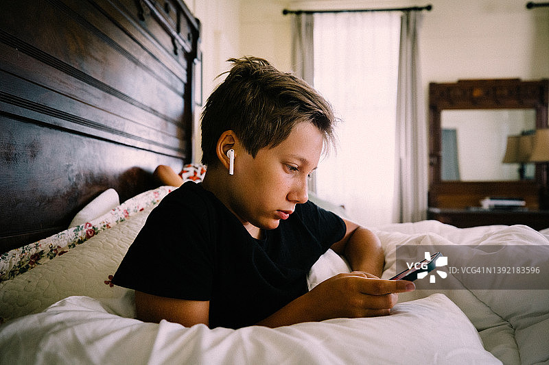 戴着耳机和拿着iPhone的青少年男孩在古董床上图片素材