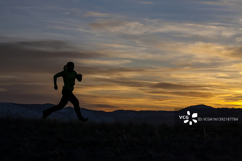 一名女子在日落时跑步，背景是群山图片素材