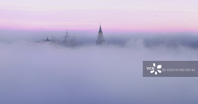 紫色日出中笼罩在薄雾中的古老教堂塔楼图片素材