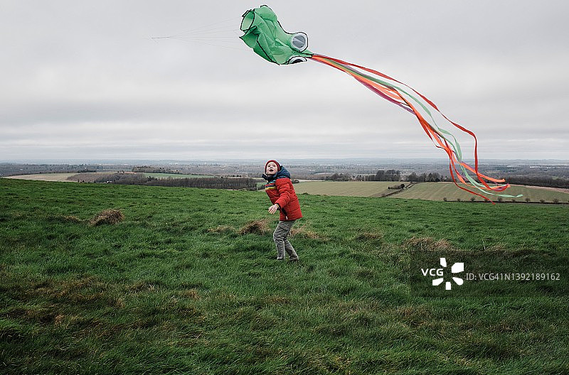 男孩在微风习习的绿色田野上放风筝图片素材