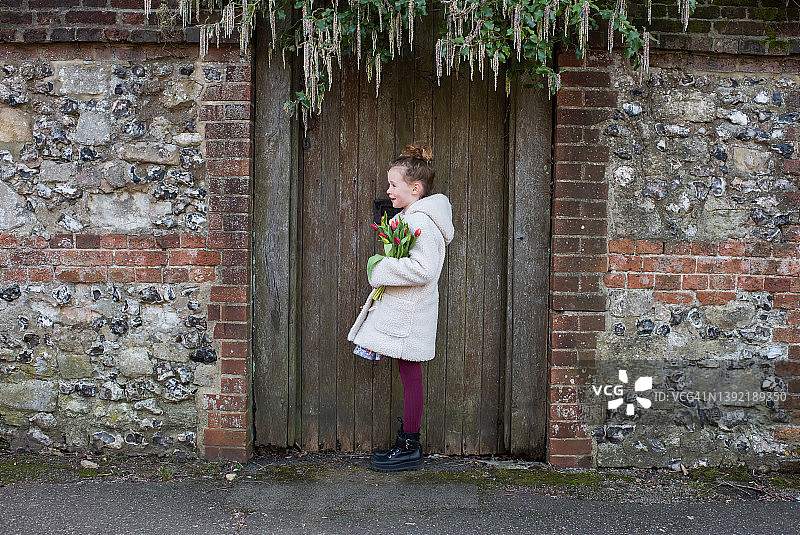 女孩拿着花站在古老的英式门旁图片素材