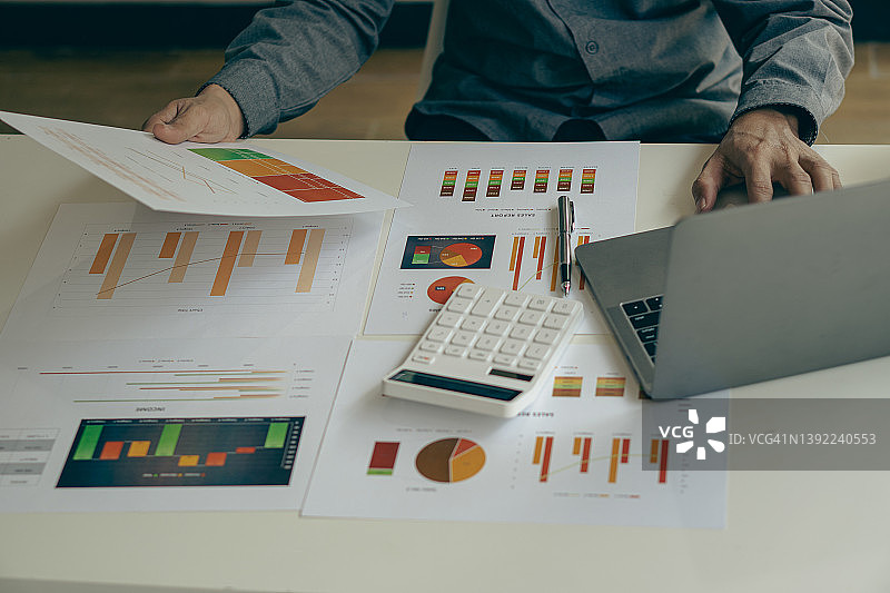 商务人士或会计手持笔和分析图表文件，计算公司预算和财务计划周转率，通过图表报告并使用笔记本电脑进行数据分析图片素材