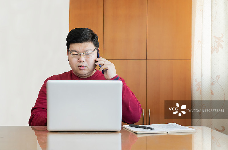 东亚男人在家使用笔记本电脑上网和打电话图片素材