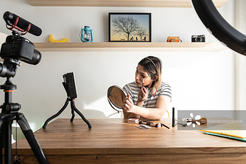年轻女人在三脚架和灯光设备旁的相机附近拍摄日常化妆教程图片素材