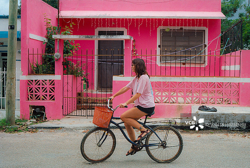 身穿粉色衬衫，骑自行车，背景是粉色建筑的女人图片素材