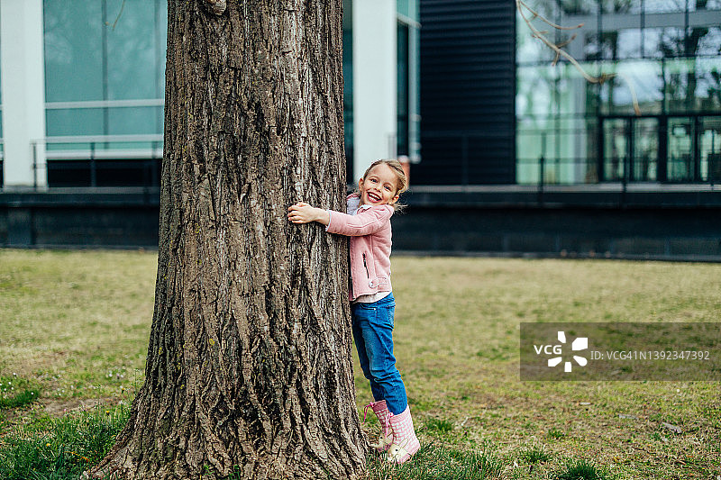 微笑的小女孩拥抱大树的树干图片素材