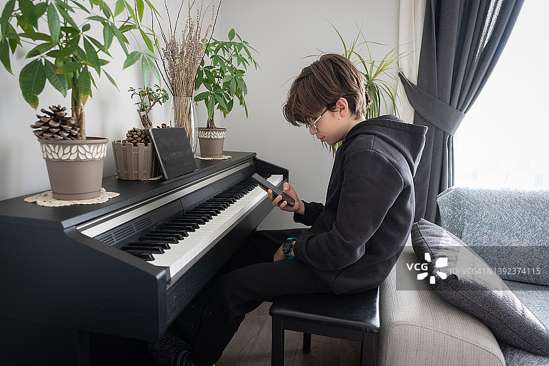 在家使用手机并练习现代数码钢琴的年轻男孩图片素材