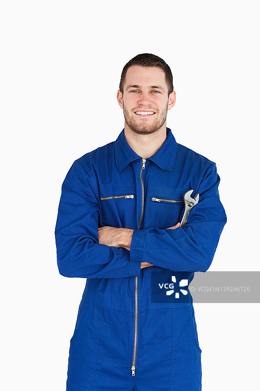 微笑的年轻技工身穿工作服，手持扳手，双臂交叉图片素材