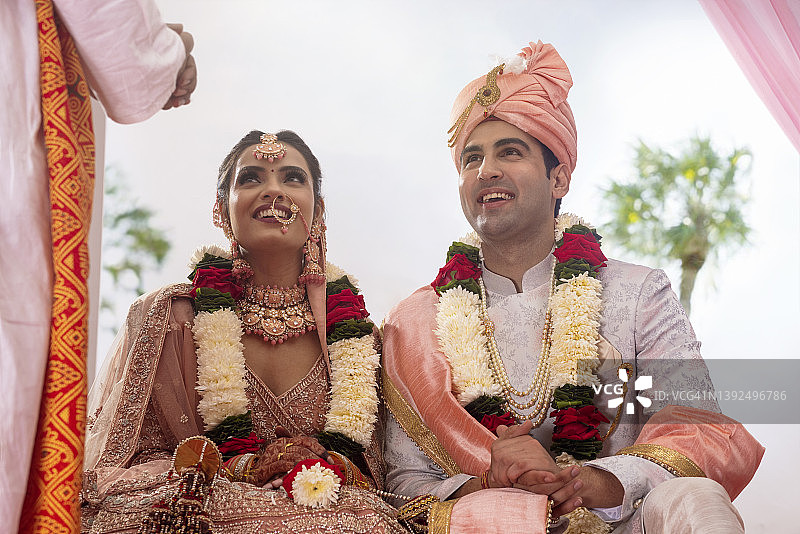 快乐的印度新娘和新郎坐在婚礼凉亭里图片素材