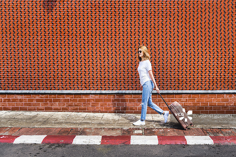 在城市人行道上拉着行李箱的女游客图片素材
