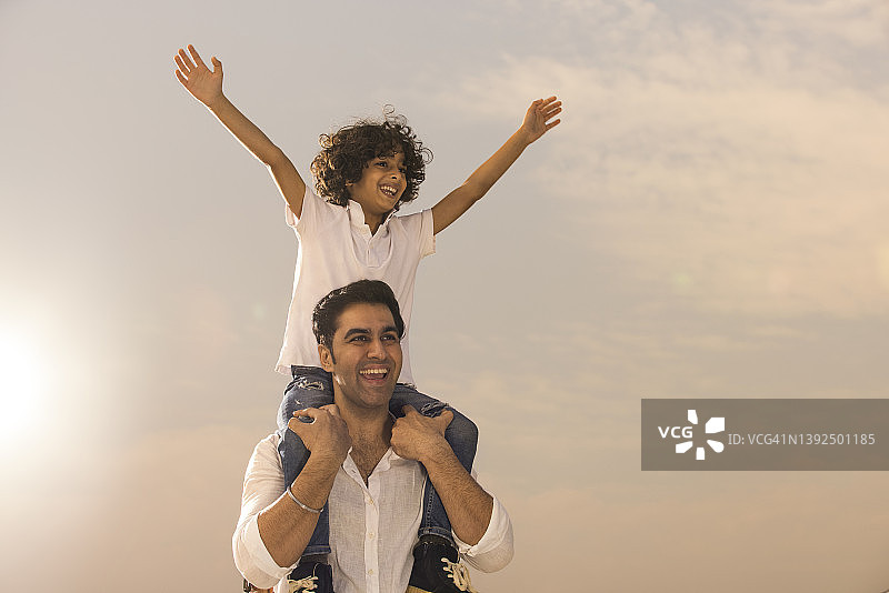 男孩坐在父亲肩膀上伸展手臂图片素材