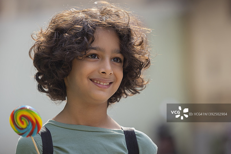 拿着彩色大棒棒糖并看向远处的儿童男孩肖像图片素材