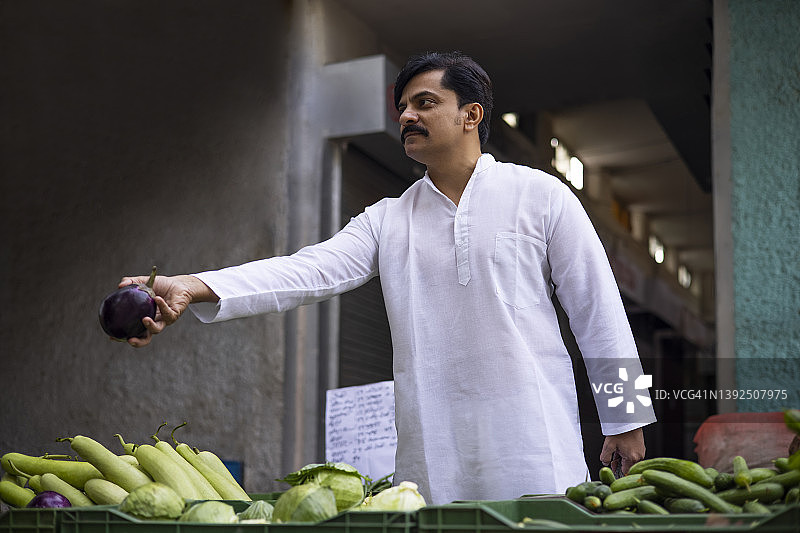 中年男子在市场上购买茄子。图片素材