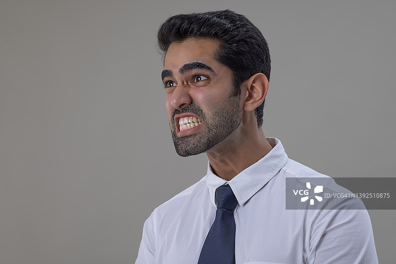 咬牙切齿、目光移开的白衬衫愤怒的年轻人图片素材