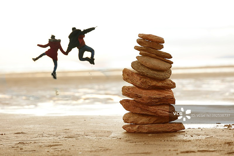 情侣在海滩石堆旁跳跃图片素材